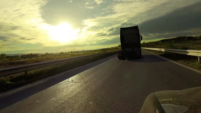 Fast truck cabin overtaking car on rural road against the sunset