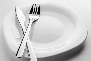 empty white plate, fork and knife on a white background.