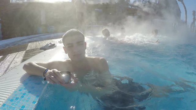 Young man relaxing in thermal pool having dring and smiling