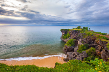 Volcanic green rock with huge stones, on the sea shore, against the backdrop of beach sunset. Beautiful blue clouds on the horizon. Balangan beach view, Jimbaran, South Kuta, Bali, Indonesia.