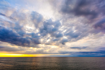 Obraz premium Beautiful bright cumulus clouds above the ocean coast before sunset. Under the cloud you can see a colorful yellow light from the sun. Balangan beach view, Jimbaran, South Kuta, Bali, Indonesia.