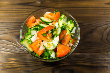 Fresh salad with tomato, cucumber, onion, parsley and dill in glass bowl on wooden table