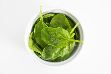 Fresh wet green baby spinach leaves, closeup on white background.