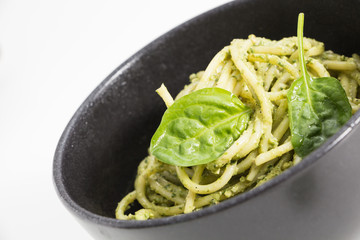 Spaghetti pasta with sauce pesto in black bowl, closeup background on white.