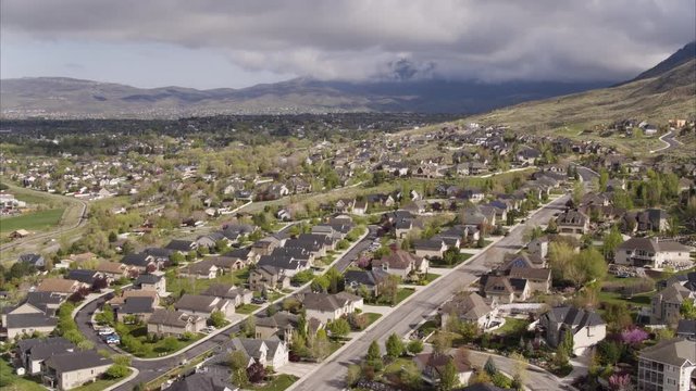 Wide high angle flyover shot of suburbs under clouds toward mountains / Cedar Hills, Utah, United States