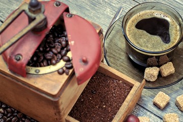 Old coffee grinder with a cup of coffee, coffee beans on a wooden background.