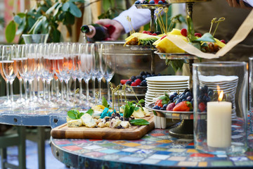 Different kinds of cheeses on wooden board, color table, wineglasses, fruits