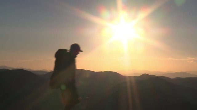 Silhouetted man walks past sun flare over mountain layers on Bald Mountain.