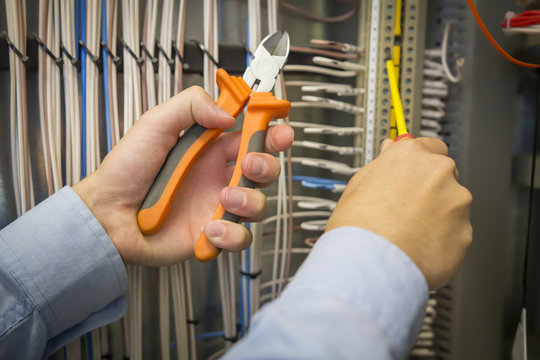 Electric installation work. Screwdriver and pliers in hands of an electrician on background of electric cabinet.