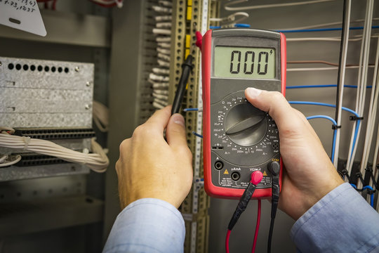Multimeter in hands of electrician engineer closeup on electric panel background. Test circuit. Service work.