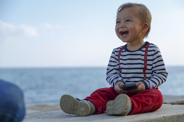 Fototapeta premium A baby boy is playing with mobile phone on a beach