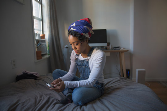 Young woman using smartphone while sitting on bed at home