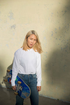 Portrait of young woman with skateboard standing against wall