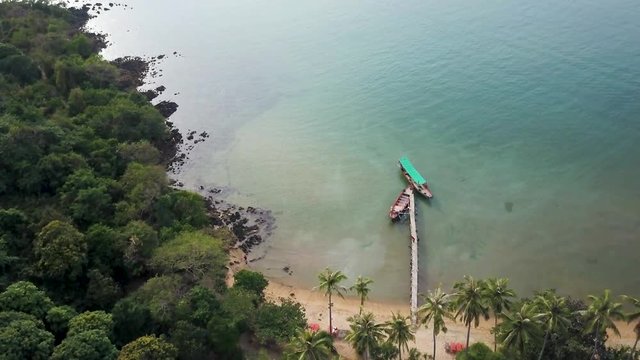 Camera tilts down showing fishing and tourist boats tied to a dock and then a lush tropical backpacker paradise with palapas.