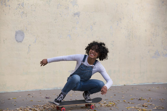 Portrait of smiling young woman skateboarding against wall