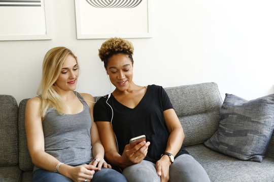 Women listening to earbuds on sofa