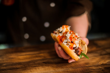 Man sitting at the wooden table holding a tasty hot dog with sausage