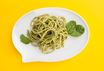 Spaghetti pasta with pesto sauce in white dish in shape of a chat bubble, on vivid yellow background.