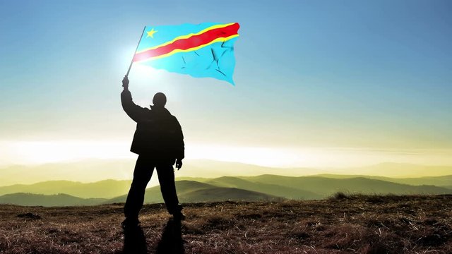 Successful silhouette man winner waving Democratic Republic of Congo flag on top of the mountain peak. Cinemagraph LOOP background