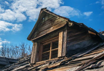 An old abandoned ruined wooden building. A roof of a destroyed house. Old attic with window. A decrepit roof