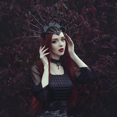A beautiful woman with pale skin and long red hair in a black dress and in the black crownk. Girl...