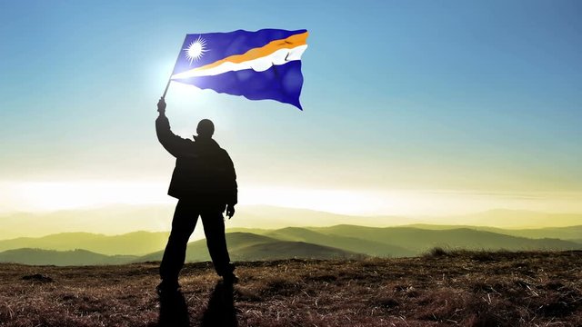 Successful silhouette man winner waving Marshall Islands flag on top of the mountain peak, Cinemagraph LOOP background