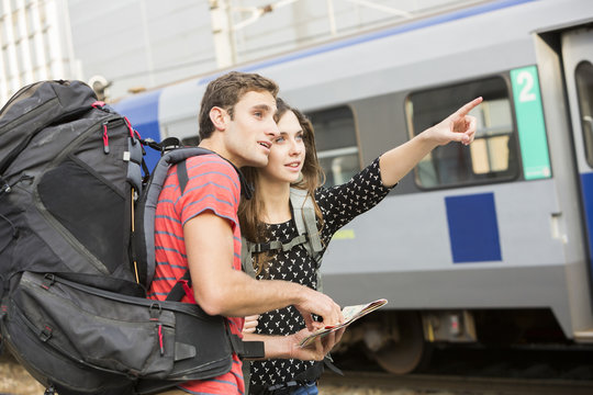 Caucasian couple reading map near train and pointing