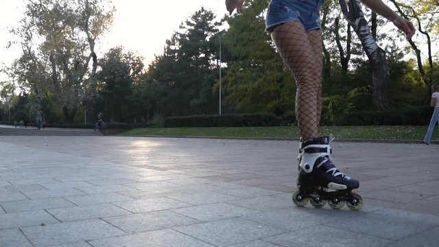 Young attractive woman in sexy tights rollerblading in park on a beautiful sunny evening. running across