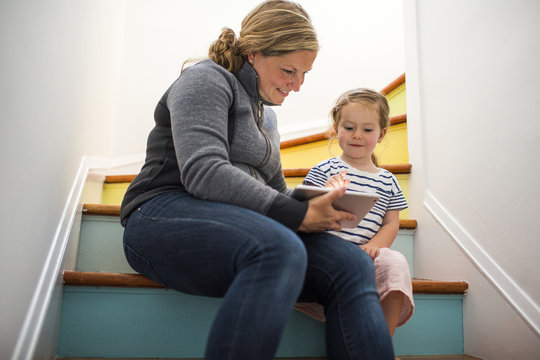 Caucasian mother and daughter using digital tablet on staircase