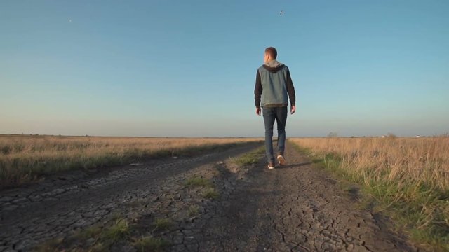 Back view of young lone man walking away down a rural road in a low angle view in a conceptual motion clip