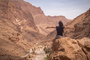 A young woman, sitting on the top of a valley, enjoying the sight and feeling happy, with her arms open. 