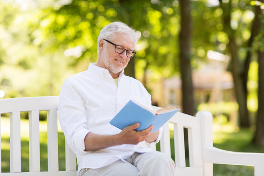happy senior man reading book at summer park
