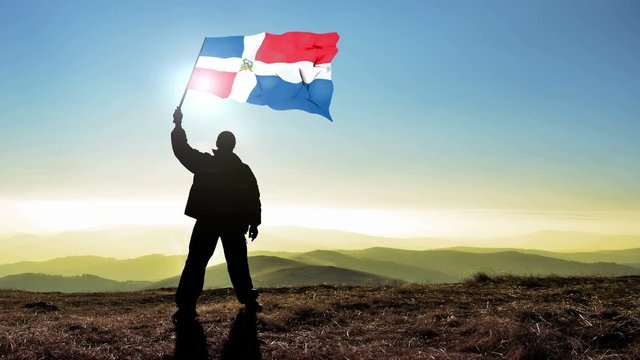 Successful silhouette man winner waving Dominican Republic flag on top of the mountain peak. Cinemagraph LOOP background
