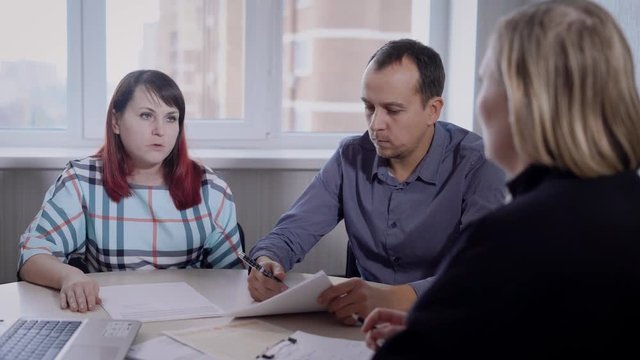adult couple is sitting on a meeting in office of real estate company, looking at a specialist, discussing