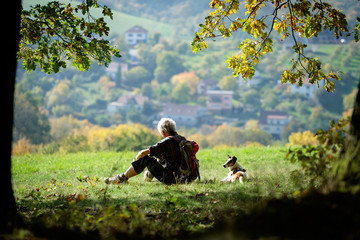 Man with his dog enjoying sunset and looking at the distance. He is wearing backpack