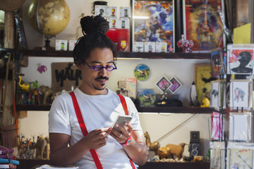 Serious mixed race man wearing suspenders texting on cell phone