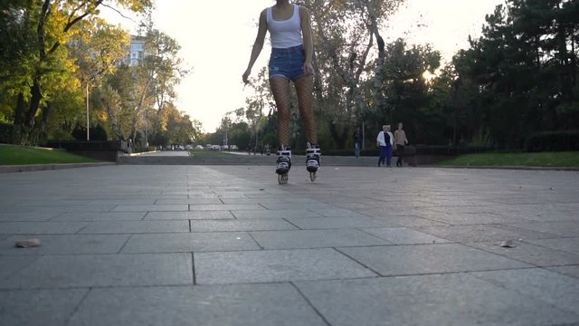 Young attractive woman in sexy tights rollerblading in park on a beautiful sunny evening. ride above the camera