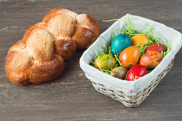 Easter wicker basket with colored eggs and Easter bread on grey wooden board.