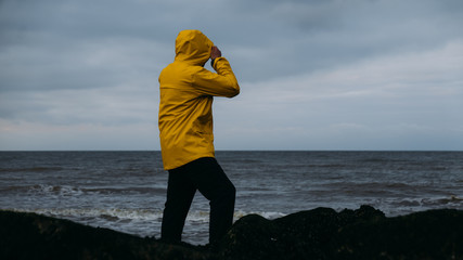 Adult Caucasian male in yellow raincoat enjoying the view of a sunset over the sea