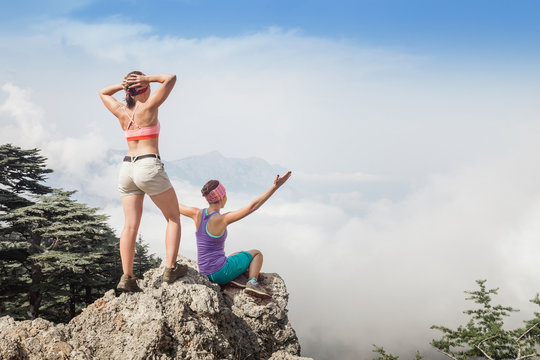 Two women stand on top of the mountain above the clouds and fog and are happy from the pottering view of the Taurus mountains near Tahtali peak, Lycian Way
