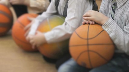 Unknown little boys sitting on their haunches and hold volley-balls in their hands, posing for photography in kindergarten indoors
