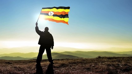 Successful silhouette man winner waving Uganda flag on top of the mountain peak, Cinemagraph LOOP background