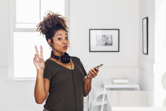 Mixed race woman holding cell phone gesturing peace