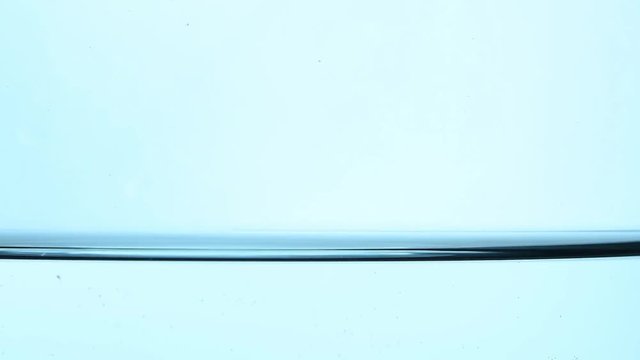 Shaking pure clear cold water surface level in transparent glass jar or teapot, close up, low angle side view, slow motion