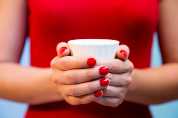Cup of tea in woman's hands with red manicure