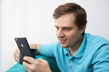 Smiling caucasian man checking his email on a smartphone and having a cup of coffee