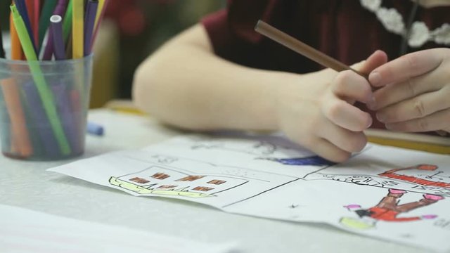 Close-up of hands of unknown little girl draws and paints pictures with felt-tip sitting at desk in the kindergarten