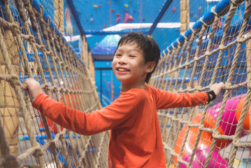 Young asian boy climbing the net at indoor playround and smiles