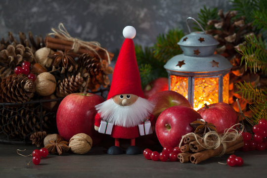 Christmas card with Santa toy. Red apples, berries, cones, nuts and a flashlight with a candle.