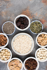 Above view of ingredients for homemade granola, oats, different nuts and raisins, dates, seed on the grey stone background, selective focus